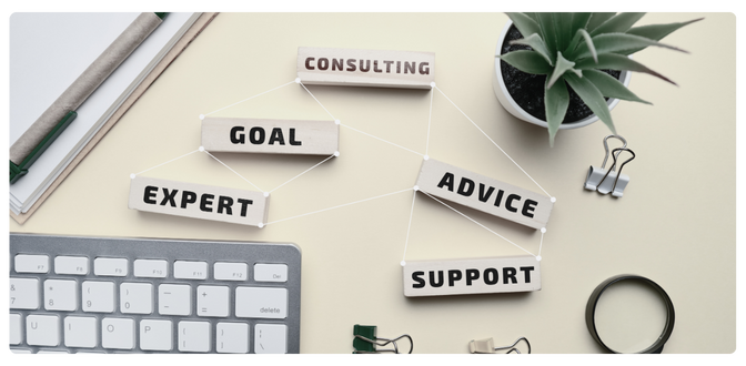 Wooden blocks with the words consulting, goal, expert, advice, and support tied together with white string and arranged on a desk with a keyboard, pen, and a plant to represent digital business consulting.